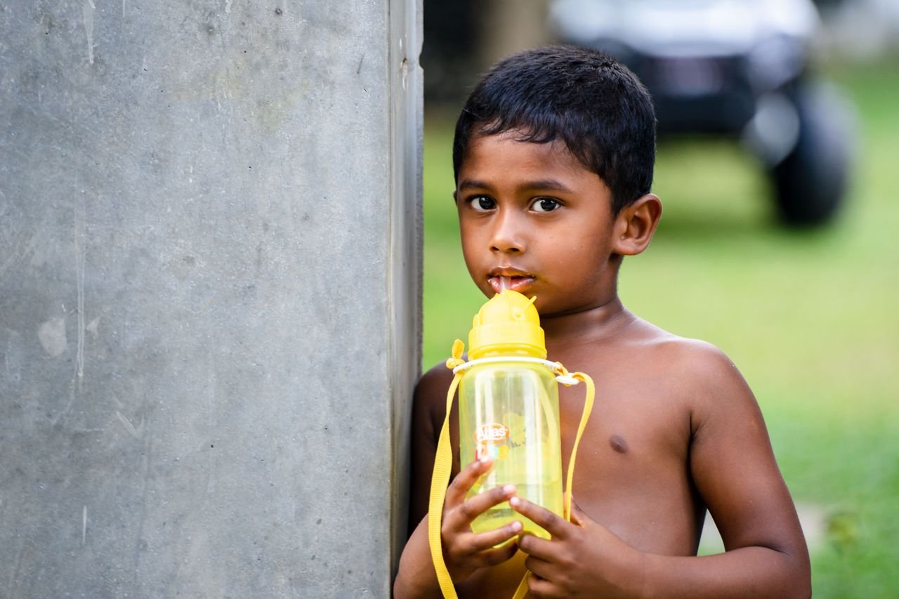 A young boy sips from a yellow tumbler, standing outdoors in Dambulla, Sri Lanka.