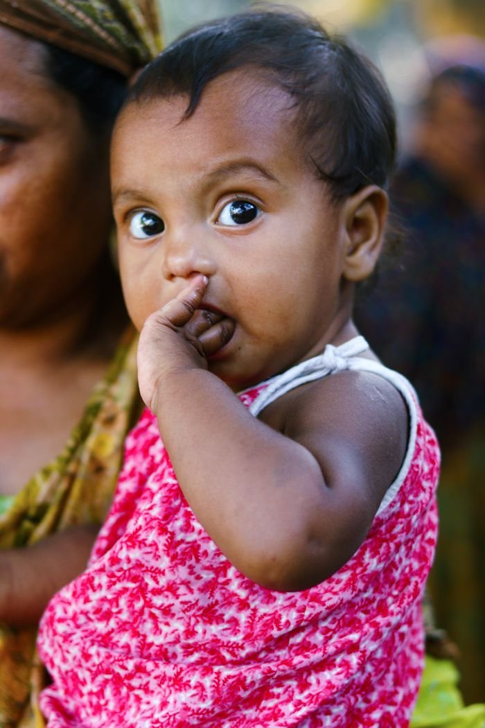 Cute South Asian baby in a colorful outfit outdoors in Bangladesh, displaying curiosity and innocence.