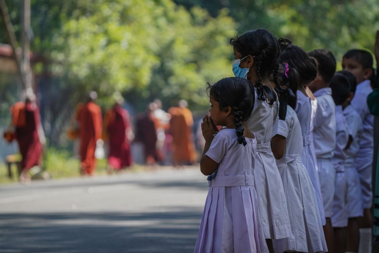 Children in white uniforms show respect during a monk procession in Sri Lanka.